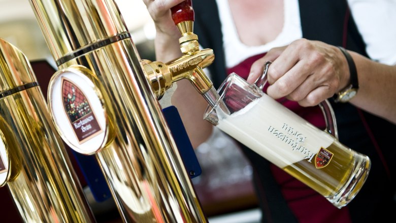 A person draws beer from a golden tap into a glass with a frothy top.