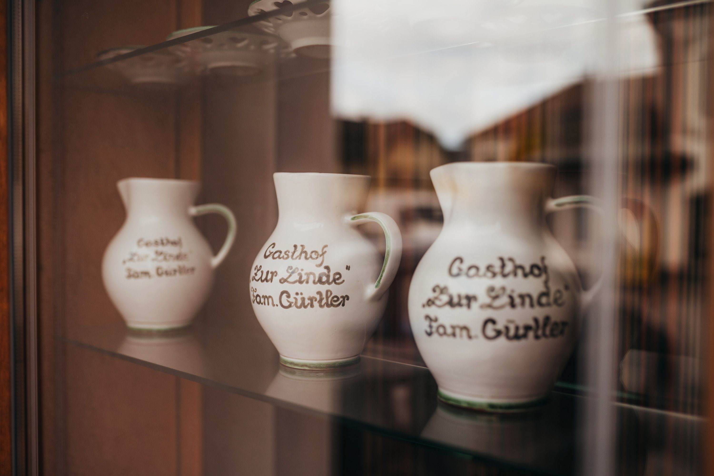 Drei Krüge mit Aufschrift "Gasthof Zur Linde Fam. Gürtler" in einer Vitrine.