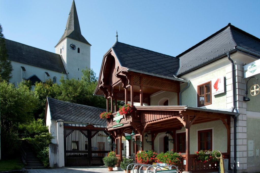 Ein traditionelles Gebäude mit Holzbalkon und Blumendekoration, daneben eine Kirche mit Turm.