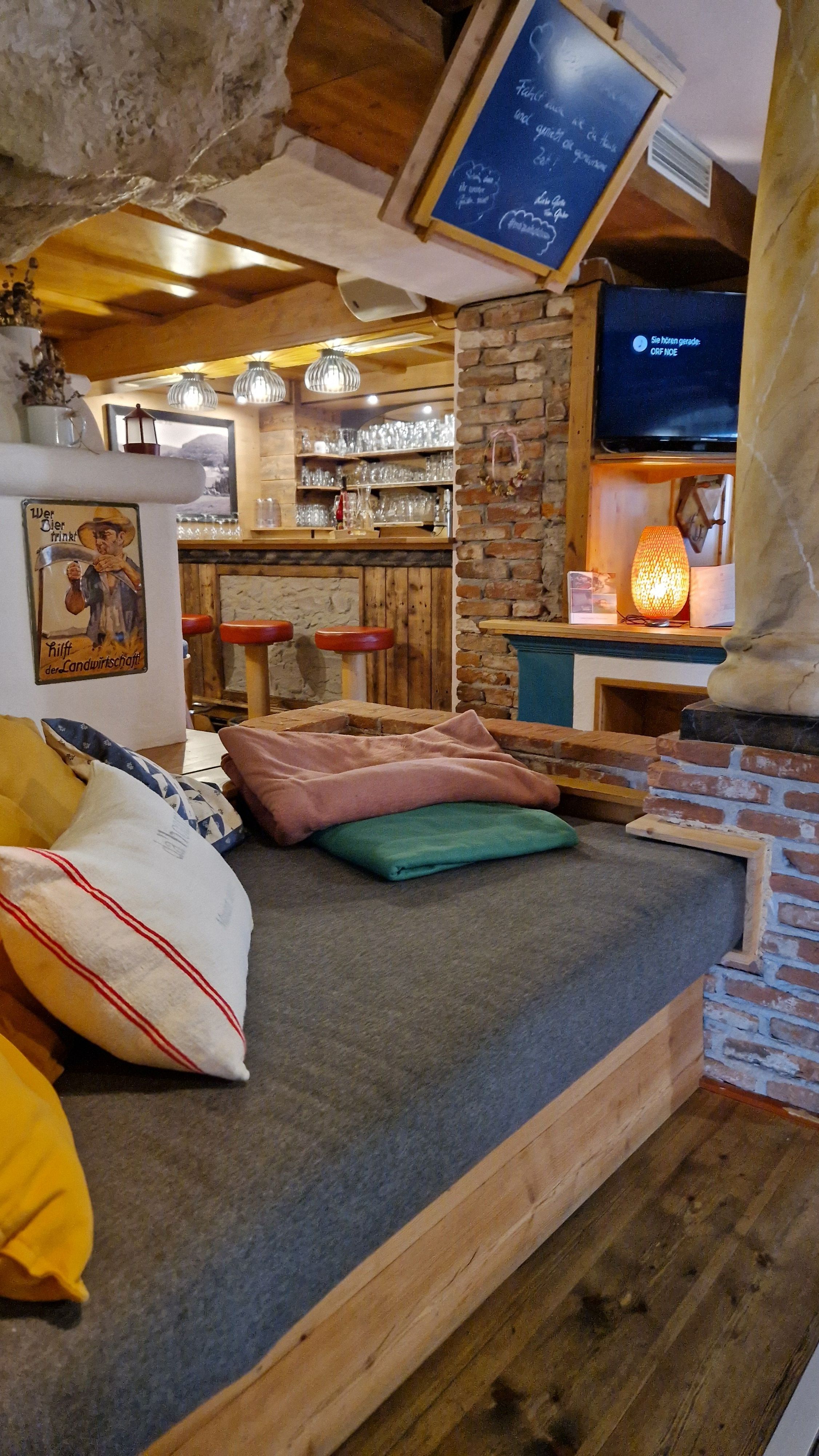 Gemütlicher Innenraum mit Holzmöbeln, Kissen und einer Bar im Hintergrund.