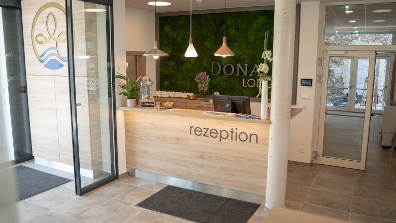 Rezeption mit Holztheke und grüner Mooswand im Hintergrund.