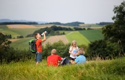 Familie macht Wanderpause entlang der Dunkelsteinerwald-Runde. Im Hintergrund erstreckt sich die Landschaft.