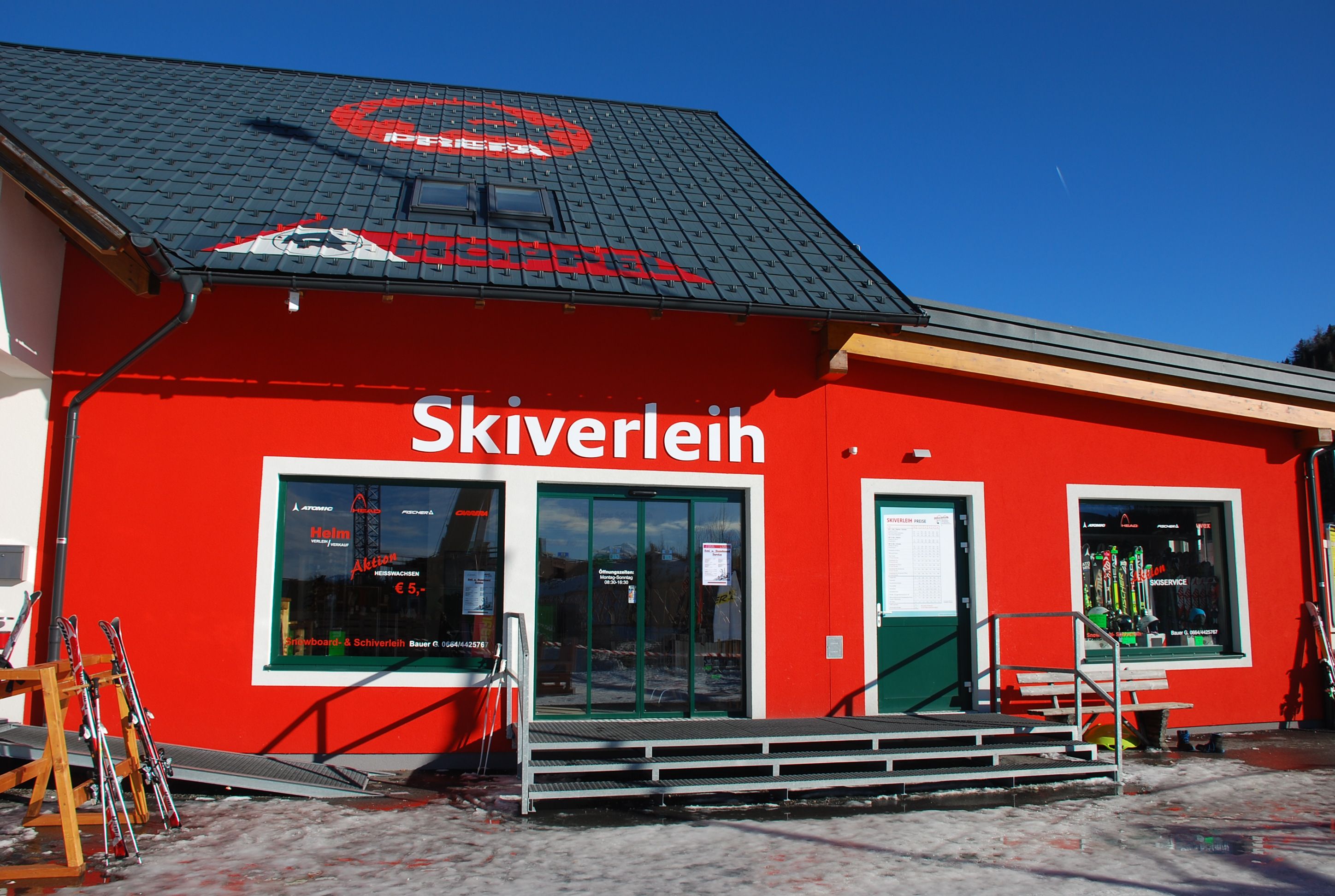 Ein rotes Gebäude mit der Aufschrift 'Skiverleih' und Skiausrüstung im Schaufenster.
