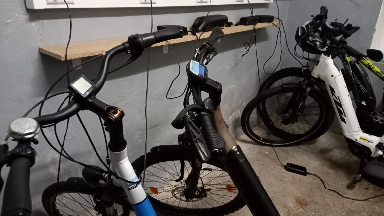 Drei E-Bikes in einer Garage, die an einer Steckdosenleiste aufgeladen werden.
