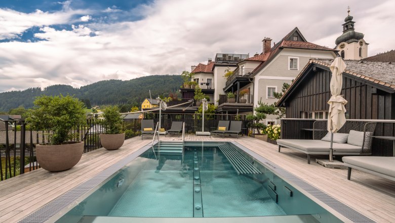 Ein moderner Pool auf einer Terrasse mit Blick auf umliegende Häuser und bewaldete Hügel im Hintergrund.