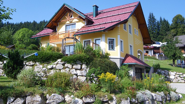 Gelbes Haus mit rotem Dach in einer gr&uuml;nen Landschaft.