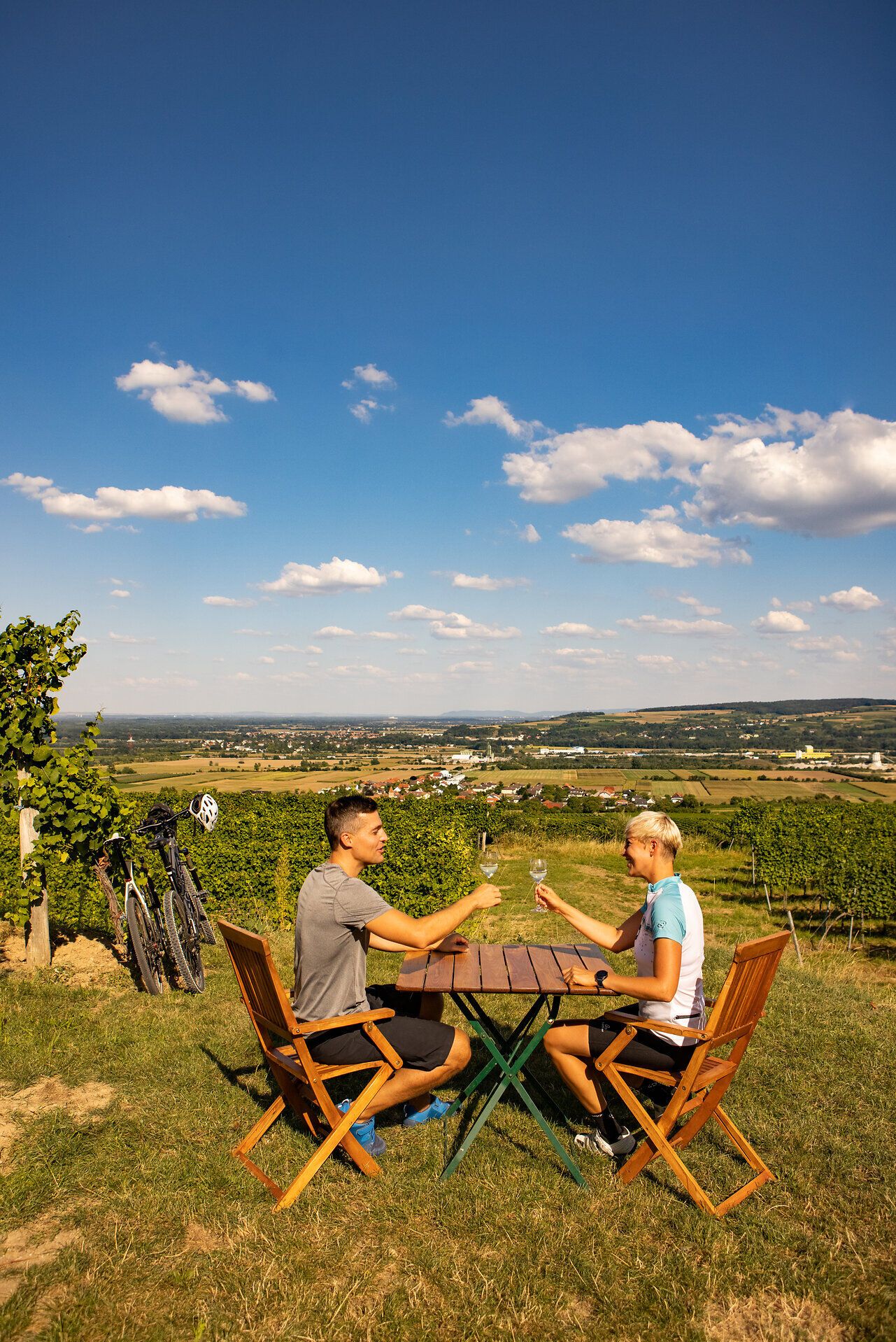 Paar sitzt an einem Tisch mit Panoramablick über Weingärten und Felder.