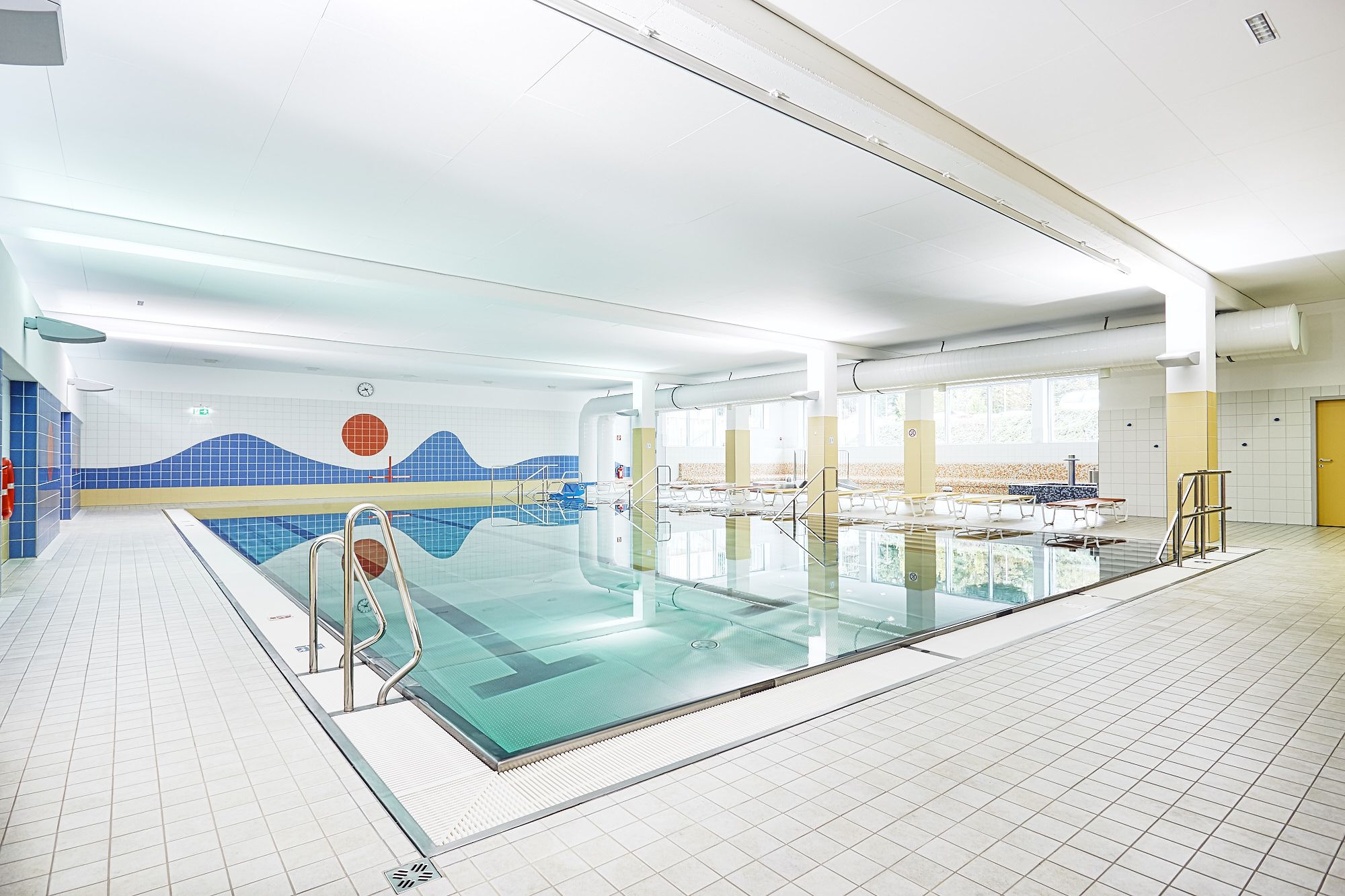 Innenansicht eines Hallenbads mit Schwimmbecken und blauer Wanddekoration.
