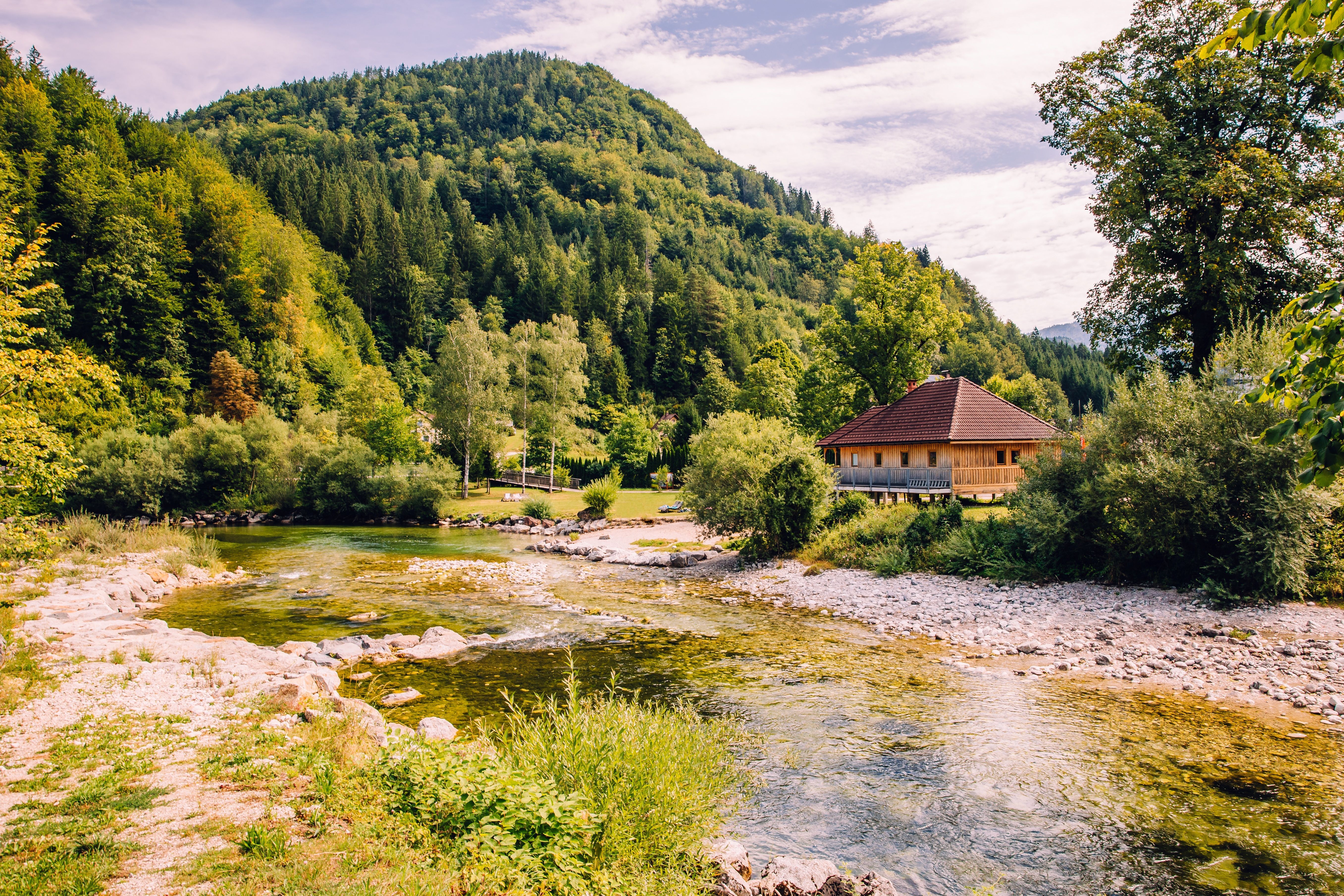 Landschaft bei Göstling: ein klarer Fluss, ein Holzhaus am Ufer und bewaldete Berge im Hintergrund.