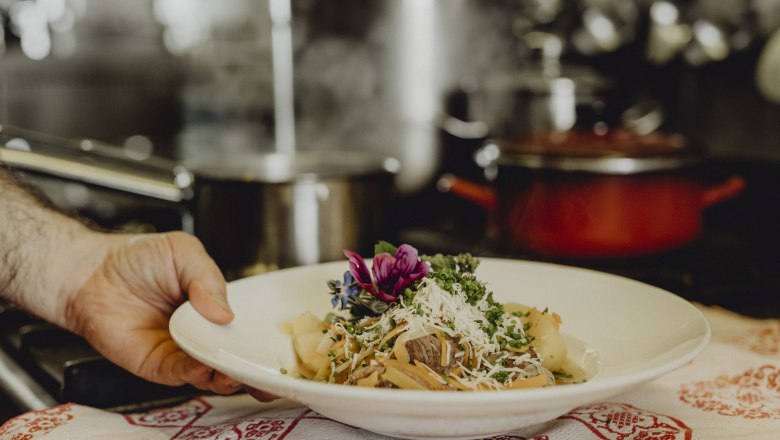 A plate of root meat, garnished with herbs and edible flowers, is served in a kitchen.