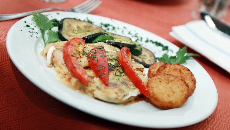 Ein Teller mit gebratenem Gemüse, Tomaten und Rösti auf einem roten Tisch.