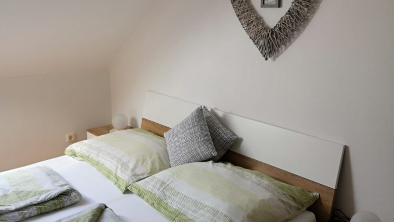 Bedroom with double bed, green bed linen and heart-shaped wall decoration.
