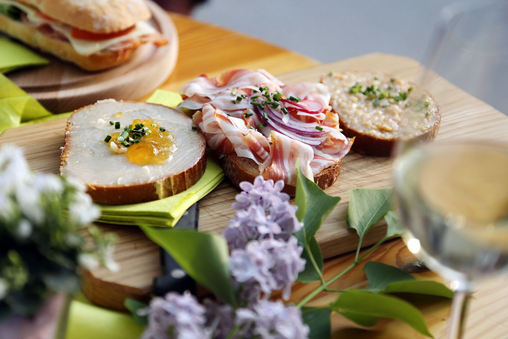 Genießen Sie die köstlichen Speisen der Heurigenjause, die auf rustikalen Holzplatten angerichtet sind. Frisch gebackenes Brot, zarter Speck und aromatische Aufstriche laden dazu ein, die Aromen der Region zu entdecken und sich in geselliger Runde zu entspannen.