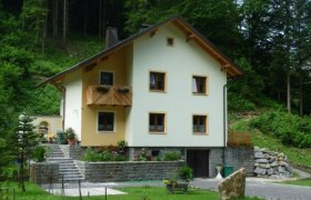 Ein gelbes Gästehaus mit Holzbalkon, umgeben von grüner Natur und Bäumen.