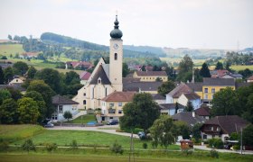 Blick auf die Marktgemeinde Ruprechtshofen mit Kirche und umliegenden Häusern in einer ländlichen Landschaft.
