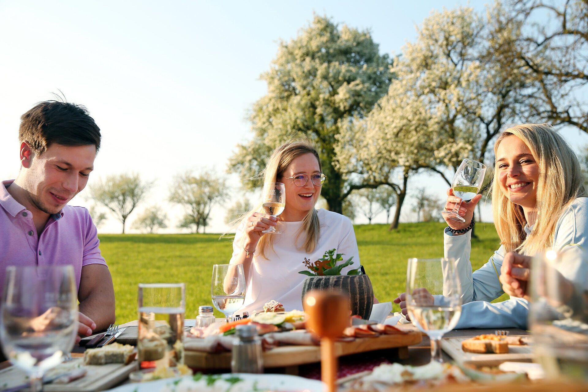 Inmitten der blühenden Birnbäume genießen Freunde einen fröhlichen Frühlingstag. Die Tafel ist reich gedeckt mit regionalen Köstlichkeiten, während die sanfte Brise die frischen Aromen verbreitet. Ein perfekter Moment, um die Schönheit der Natur und die Geselligkeit zu feiern.