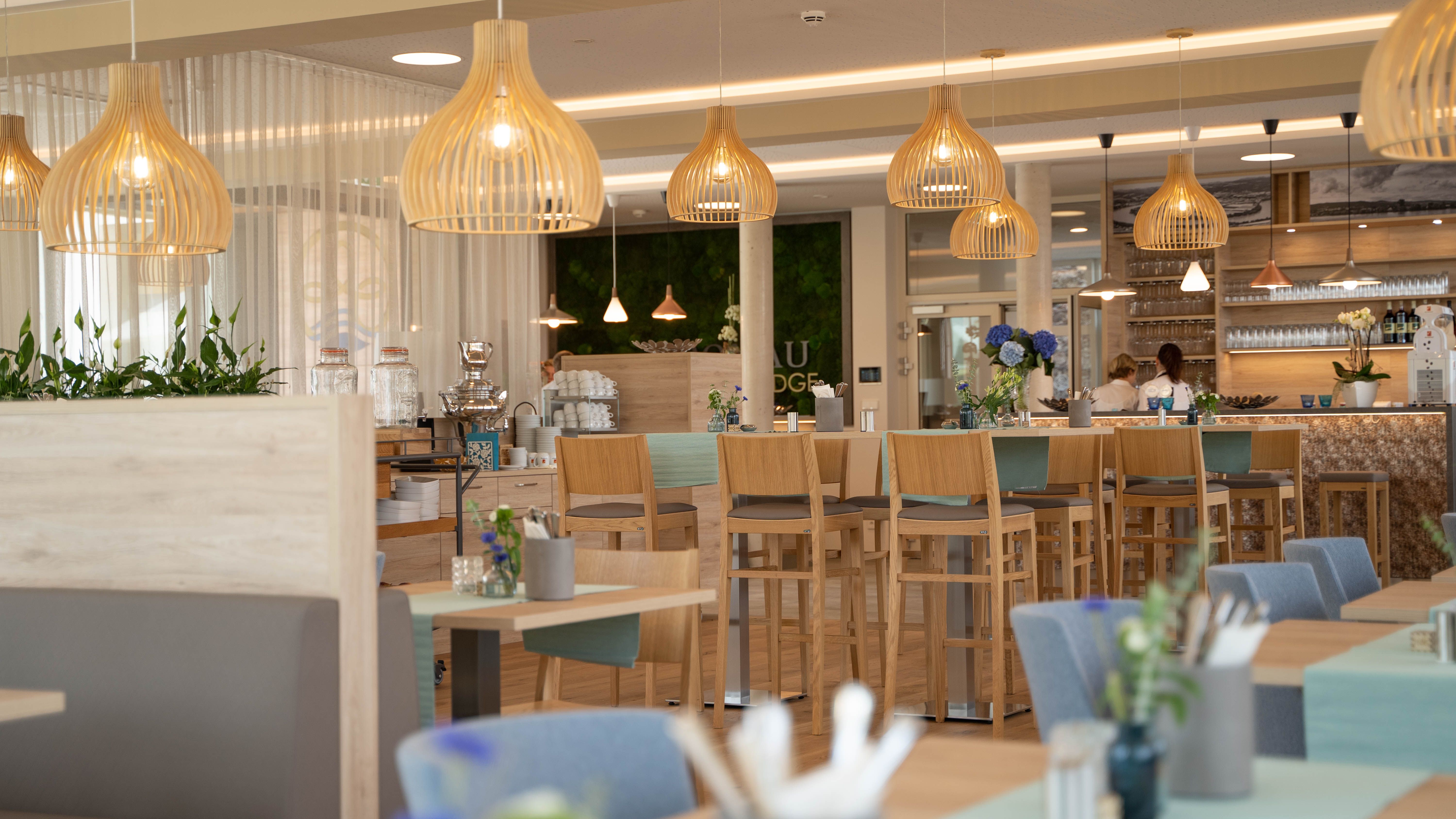 Innenansicht eines modernen Cafés mit Holzmöbeln und hängenden Lampen.