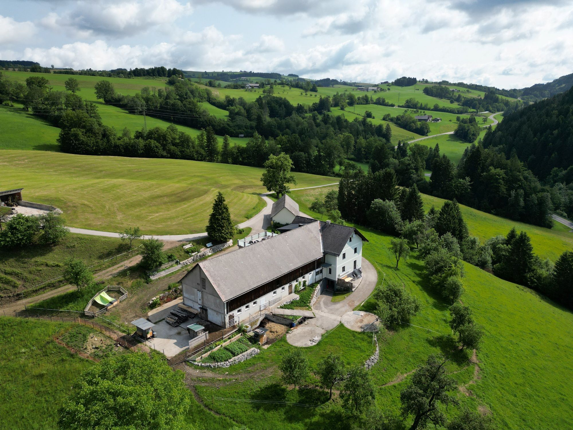 Luftaufnahme eines Bauernhofs inmitten grüner Hügel und Wiesen.