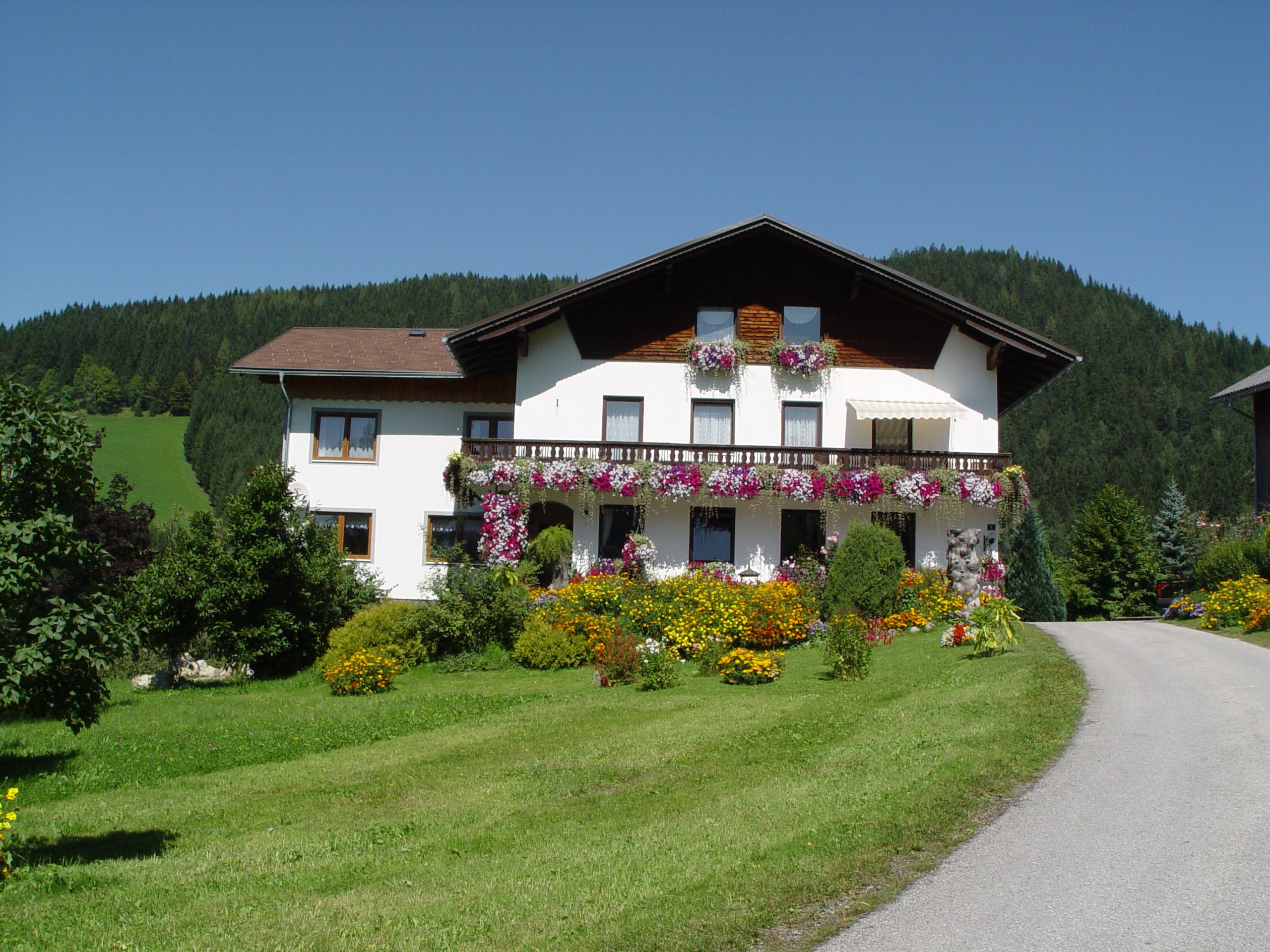 Ein weißes Haus mit Blumenbalkonen vor einem bewaldeten Hügel.