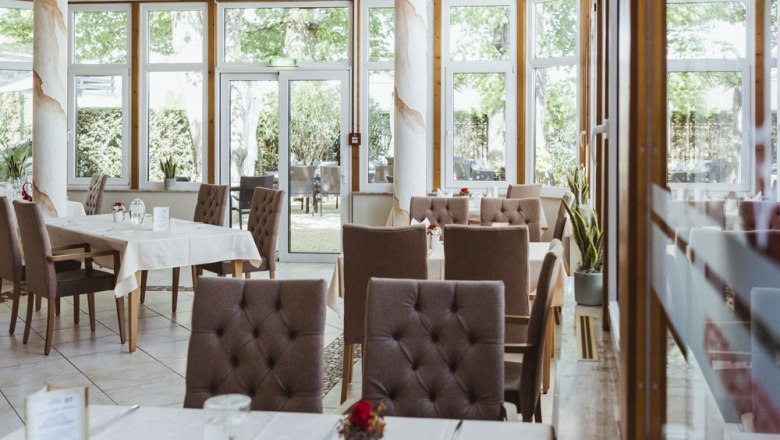 Innenansicht eines eleganten Restaurants mit gedeckten Tischen und großen Fenstern.