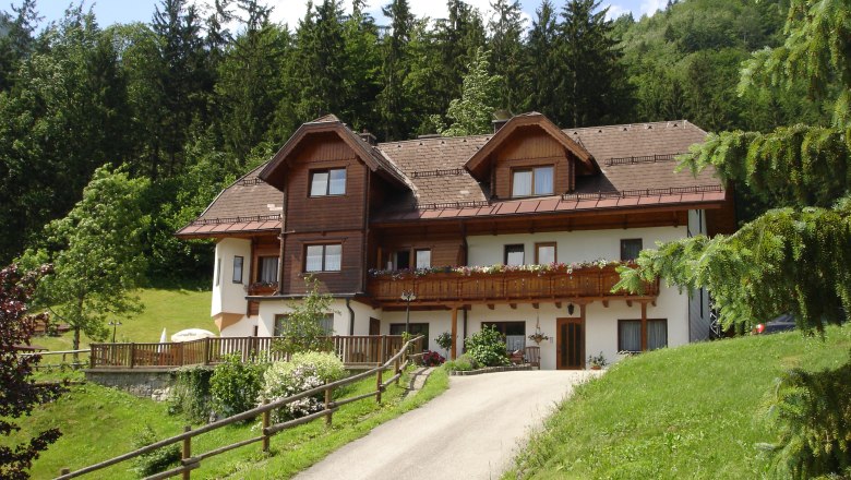 Haus Esletzbichler, © zVg Ein traditionelles Haus mit Holzverkleidung in einer grünen, bewaldeten Umgebung.