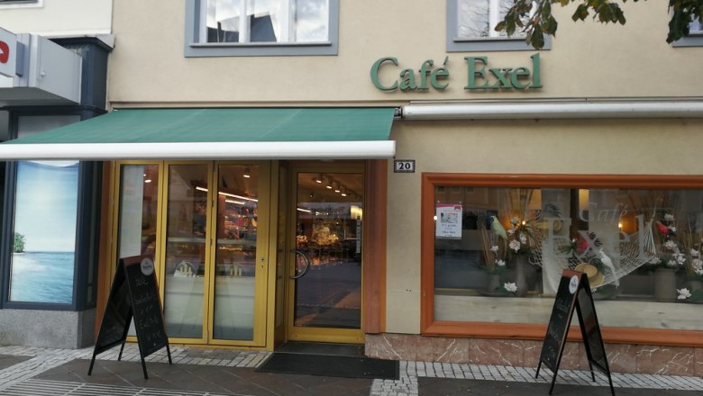 Außenansicht des Café Exel mit grüner Markise und Schaufensterdekoration.
