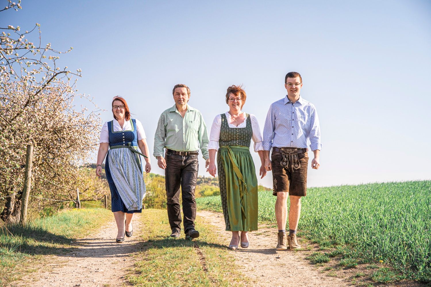 Vier Personen in traditioneller Kleidung gehen auf einem Feldweg.