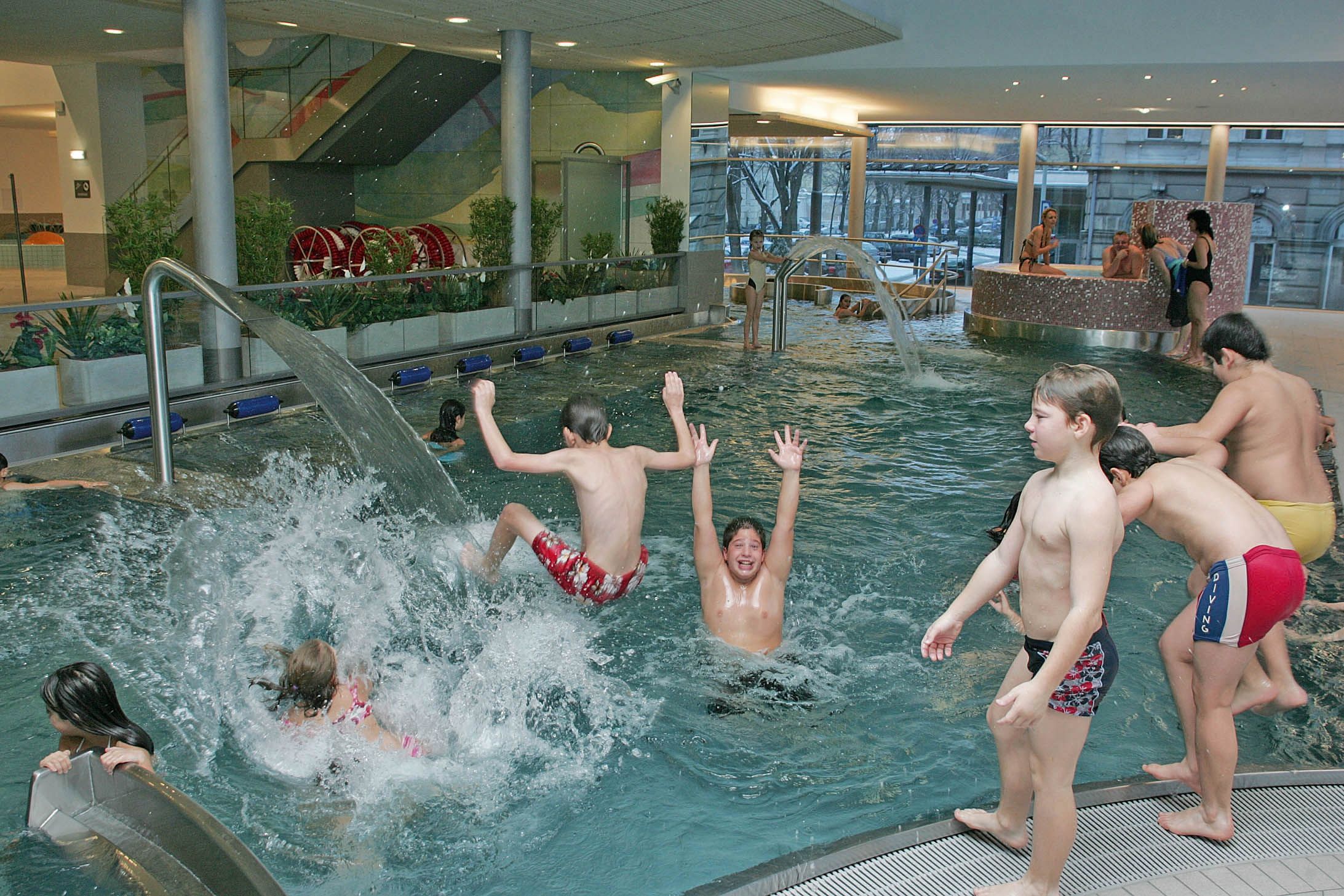 Kinder spielen und planschen in einem Hallenbad mit Wasserspielen.