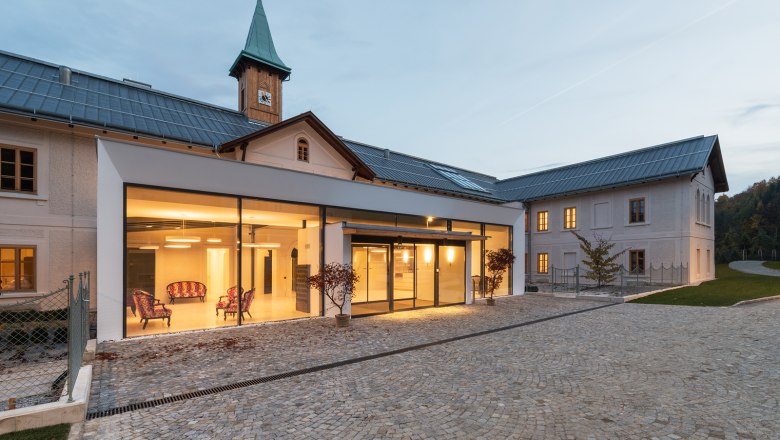 Modernes Gebäude mit Glasfassade und historischem Turm im Hintergrund.