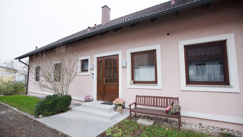 Entrance to a pink-painted vacation apartment with a wooden door, two windows and a wooden bench next to it.