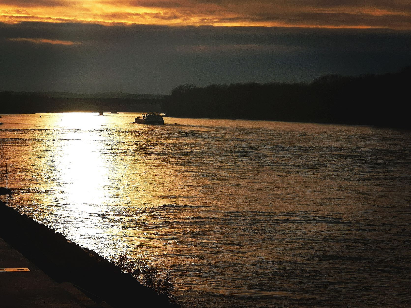 Sonnenuntergang über einem Fluss mit einem Boot im Hintergrund.