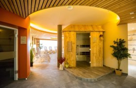 Innenansicht einer Saunalandschaft mit Holzsauna und Liegestühlen.