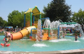 Kinder spielen in einem Wasserspielgarten mit Rutschen und Wasserfontänen.