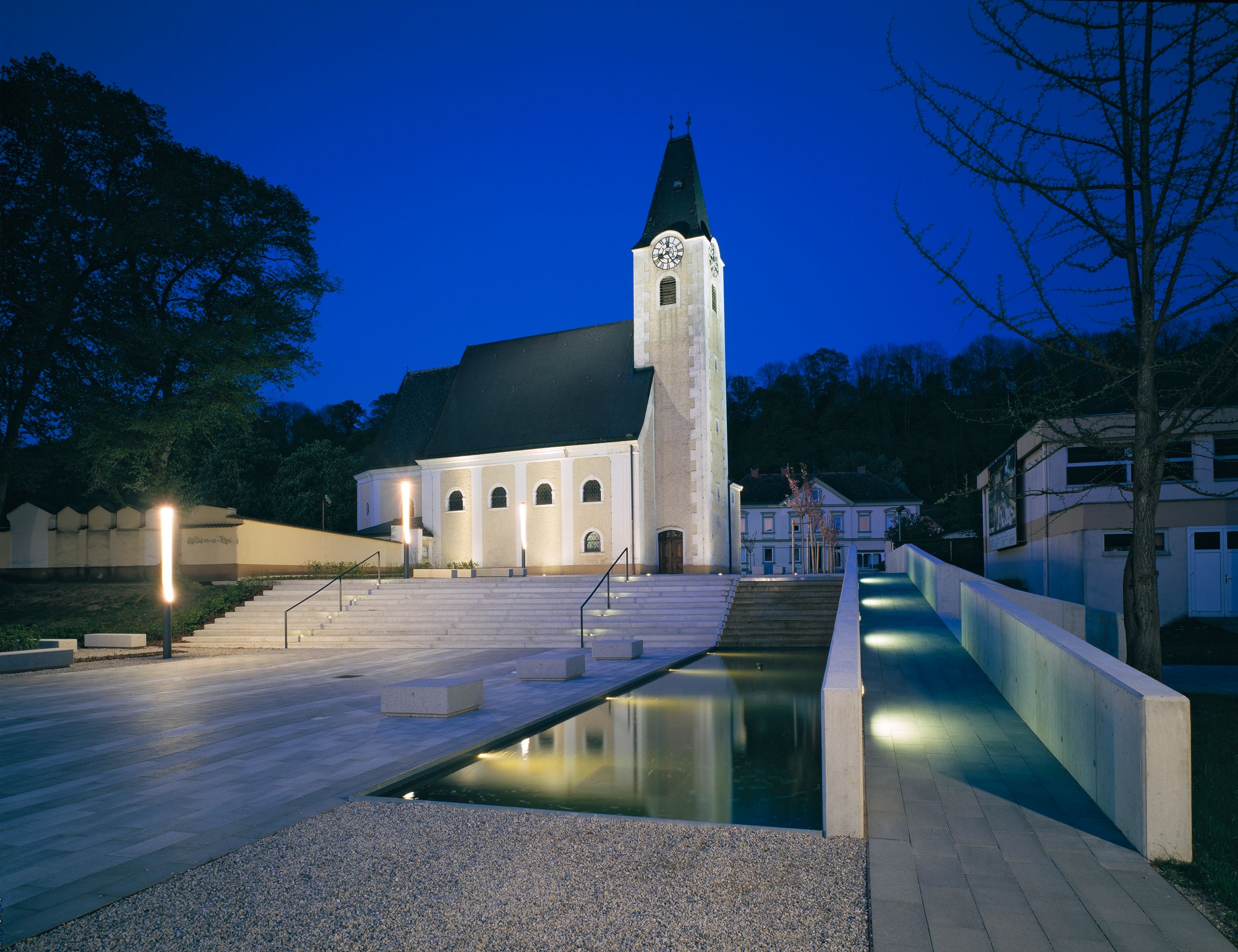 Abendaufnahme eines beleuchteten Kirchenplatzes mit Treppen und Wasserbecken in Ernsthofen.