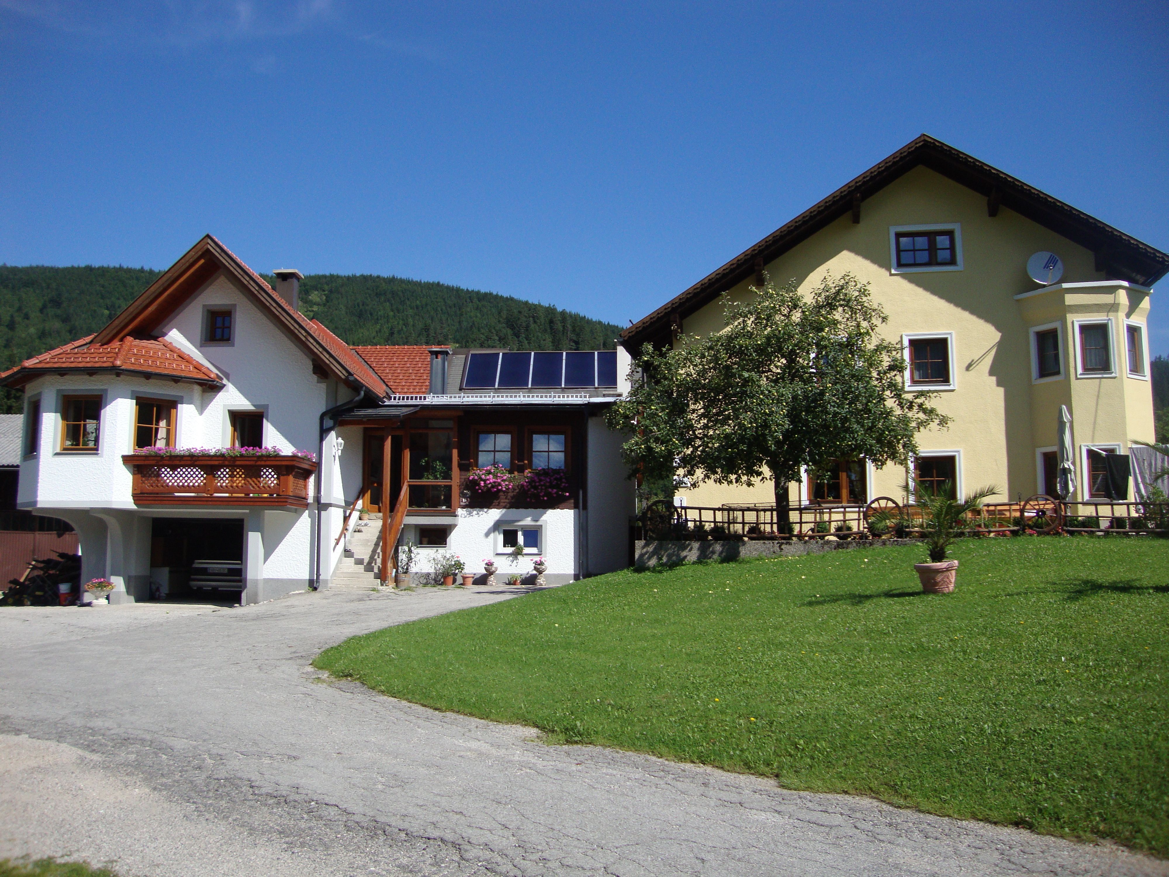 Zwei Häuser mit Garten und blühenden Pflanzen, blauer Himmel im Hintergrund.