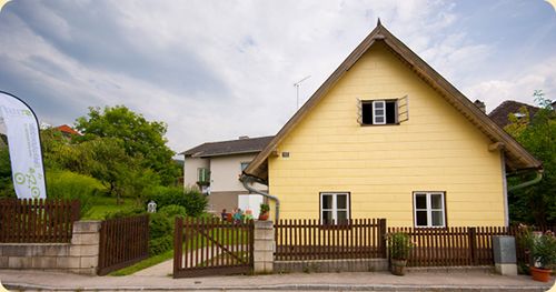 Ein gelbes Haus mit Spitzdach und Holzzaun in einer ländlichen Umgebung.