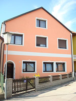 Vorderansicht eines zweistöckigen Hauses mit orangefarbener Fassade und weißen Fensterrahmen.