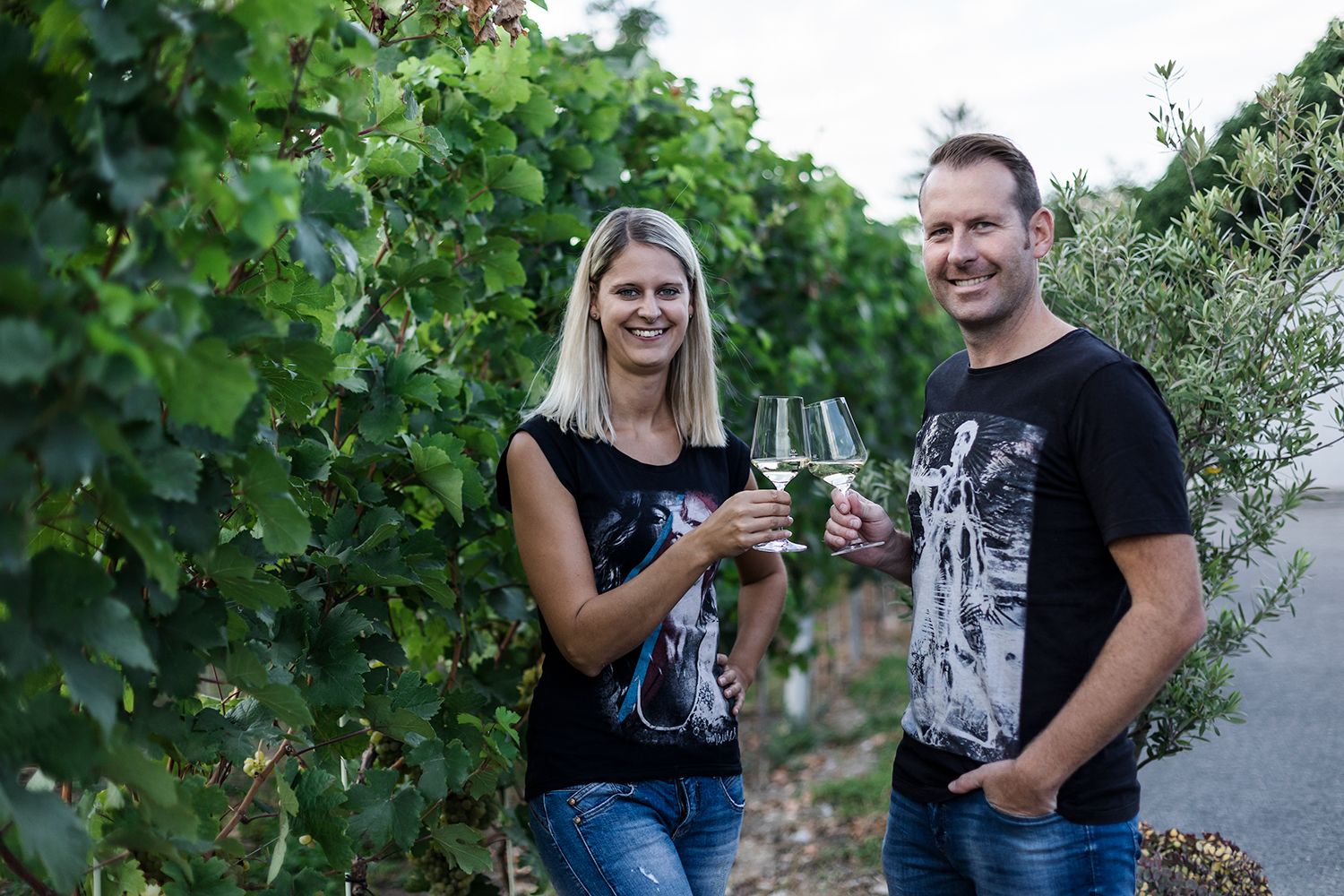 Zwei Personen stoßen mit Weingläsern in einem Weinberg an.