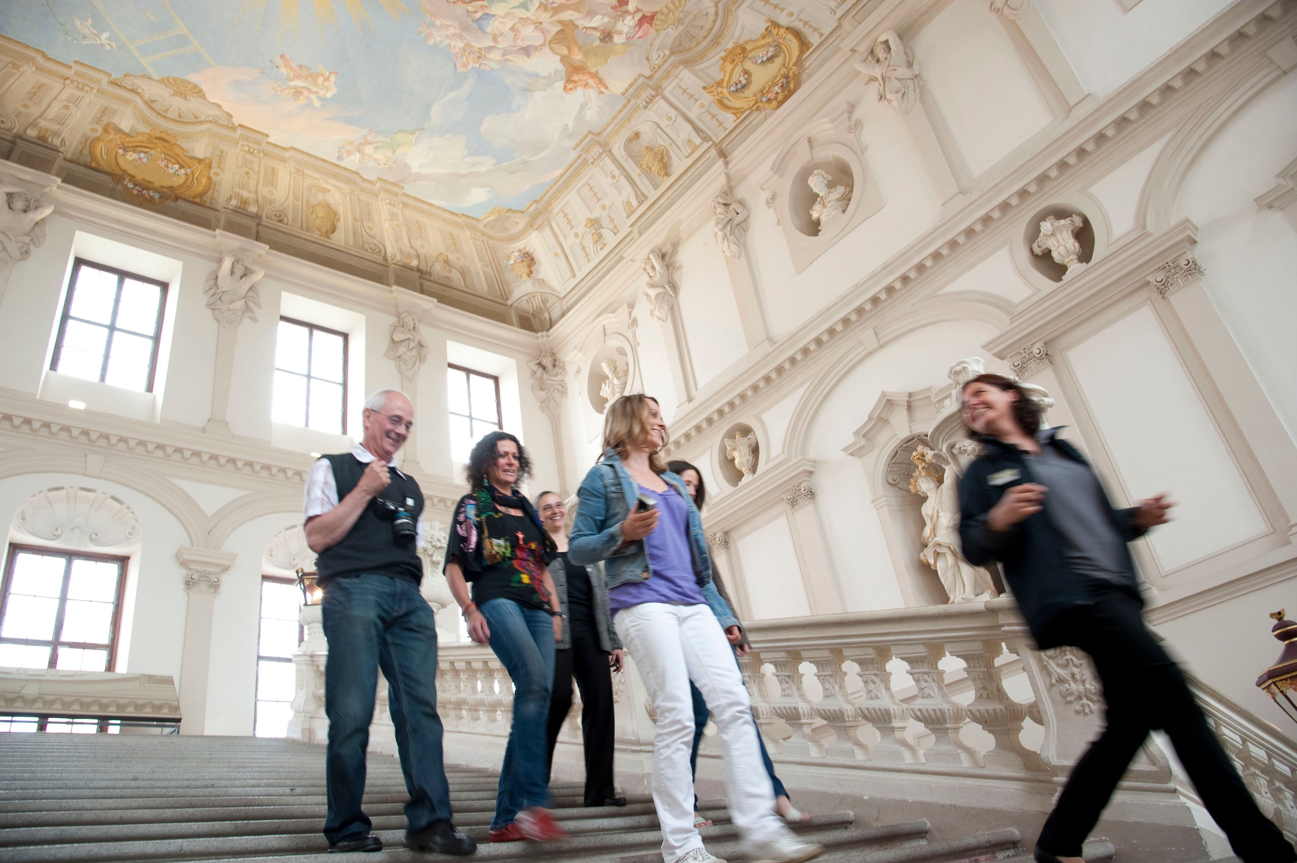 Gruppe von Menschen geht eine Treppe in einem barocken Gebäude hinunter.