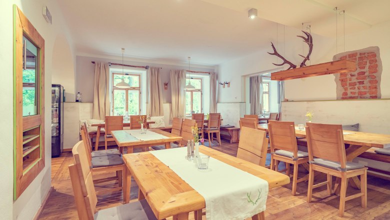 Ein rustikal-moderner Raum mit Holzmöbeln, weißen Wänden und großen Fenstern. Ein Geweih hängt als Dekoration von der Decke.