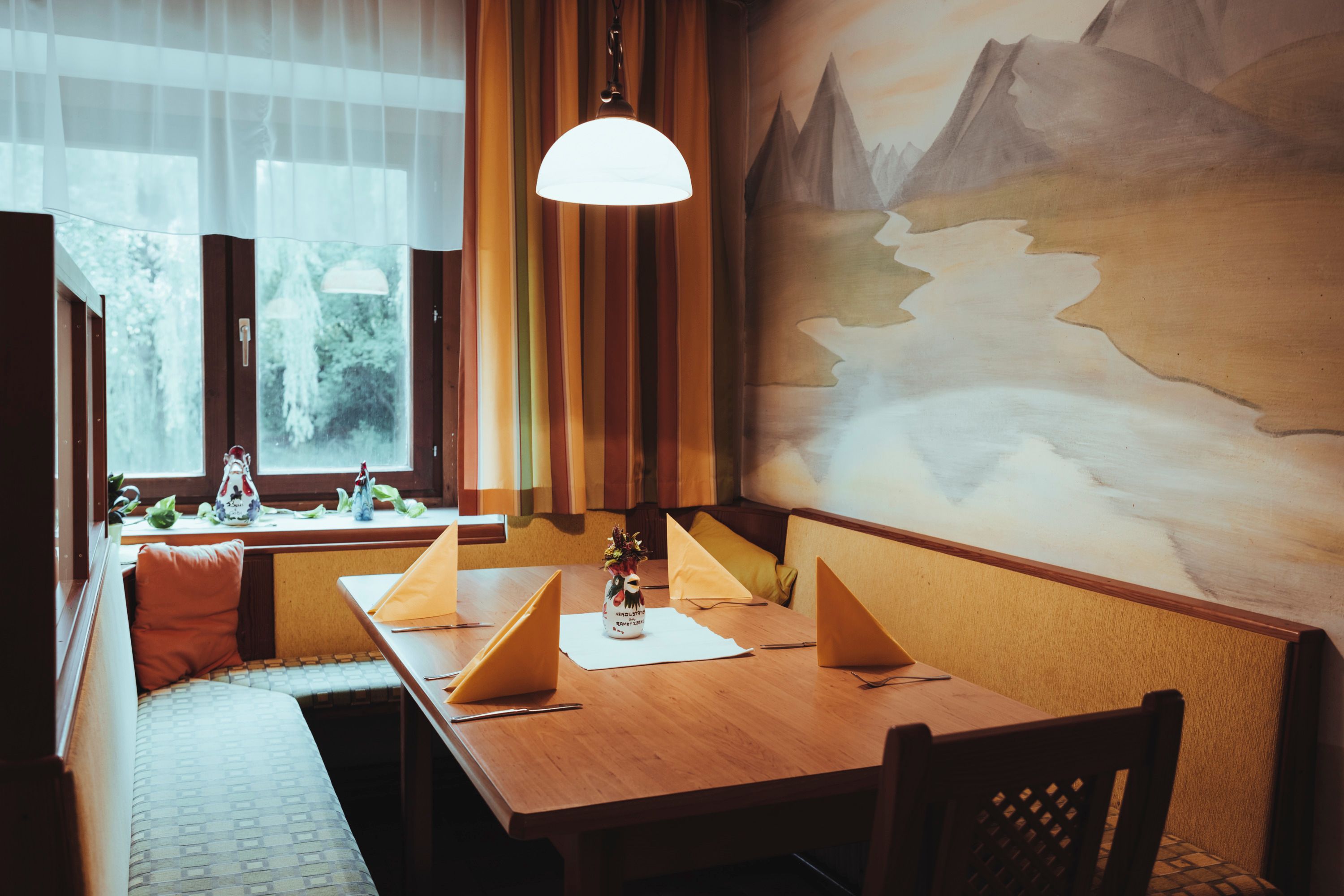 Gemütliche Sitzecke mit Holztisch, gelben Servietten und Wandgemälde in einem Restaurant.