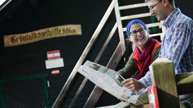 Zwei Personen sitzen vor der Gr&uuml;ntalkogelh&uuml;tte und schauen auf eine Karte.