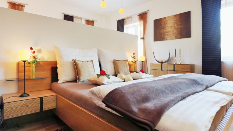 Straußenhof Ebner, © weinfranz.at Gemütliches Schlafzimmer mit Doppelbett, dekoriert mit Kissen und Rosen, Holzmöbeln und sanfter Beleuchtung.