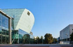 Die moderne Architektur strahlt eine harmonische Verbindung von Glas und Beton aus, während die klare, blaue Himmel die Szenerie erhellt. Umgeben von üppigem Grün lädt dieser Ort zum Verweilen und Entspannen ein, perfekt für einen Ausblick auf die Schönheit der Umgebung.