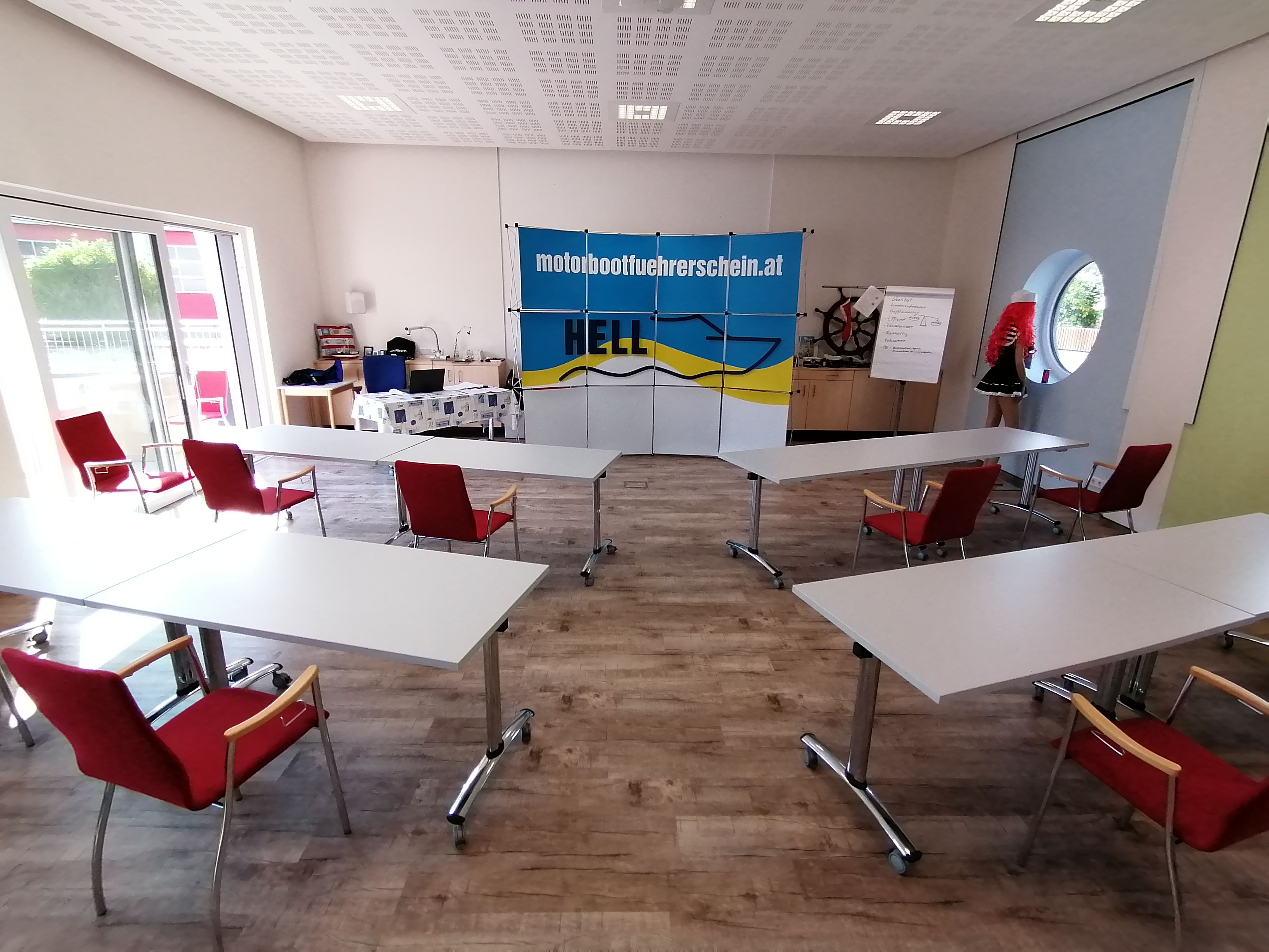 Schulungsraum mit Tischen und Stühlen, Banner der Schiffsführerschule Hell, Flipchart und Schaufensterpuppe.