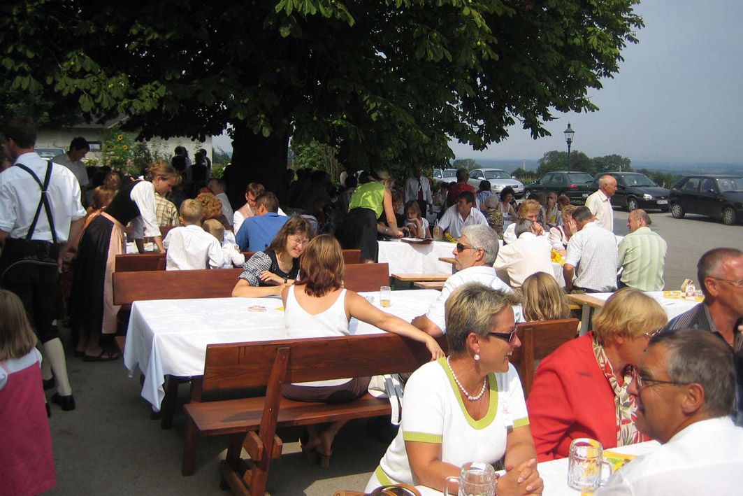 Menschen sitzen an langen Tischen im Freien unter einem Baum.