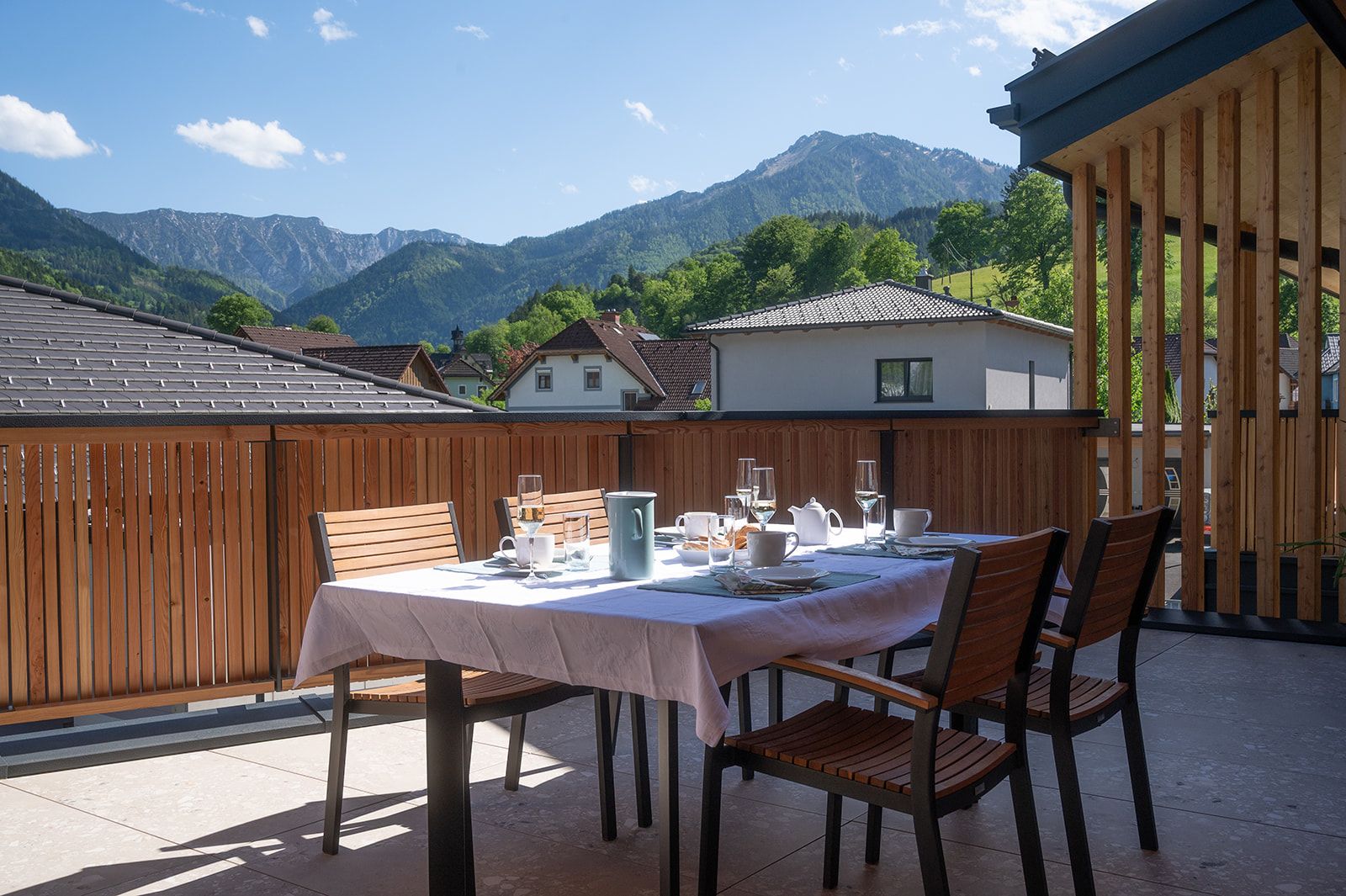 Ein gedeckter Tisch auf einer Terrasse mit Blick auf Berge und Häuser.