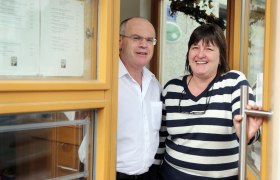 Ein Mann und eine Frau stehen lächelnd in einer Türöffnung eines Gebäudes.