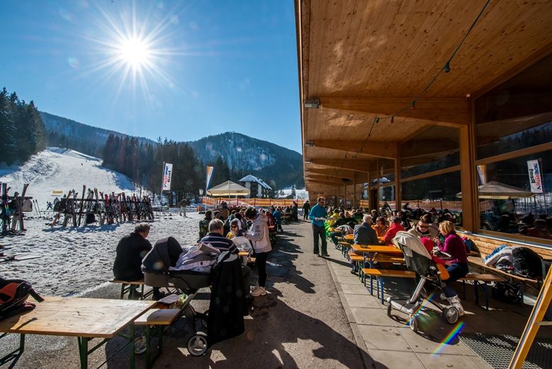 Menschen sitzen im Freien vor einem Restaurant in einem Skigebiet.