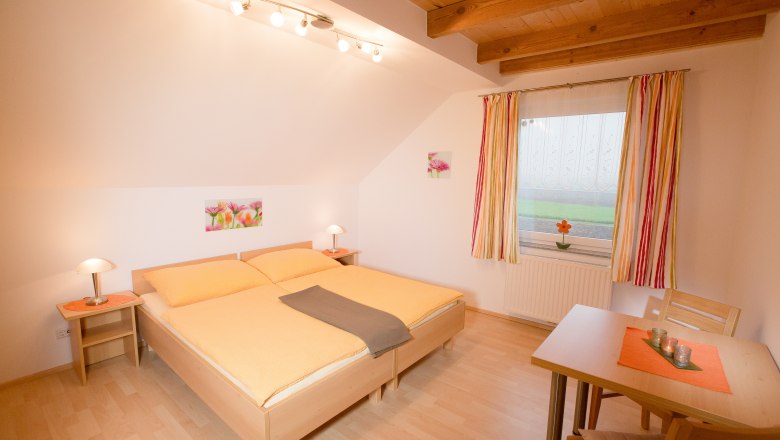 Gemütliches Schlafzimmer mit Doppelbett, Holzbalkendecke und Tisch mit Stühlen.